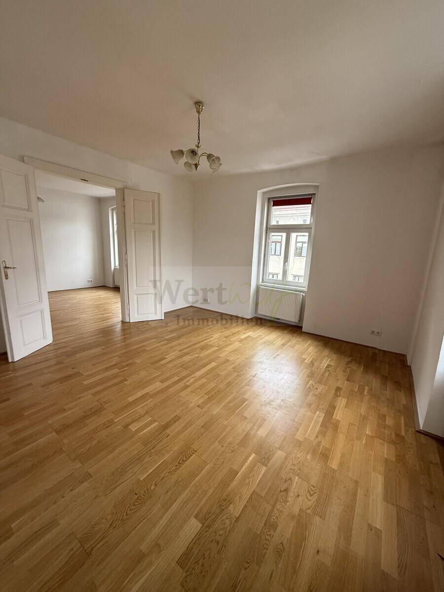 Großzügiger Raum mit Parkettboden und breitem Durchgang zu einem weiteren Zimmer, ideal für offenes Wohnen.