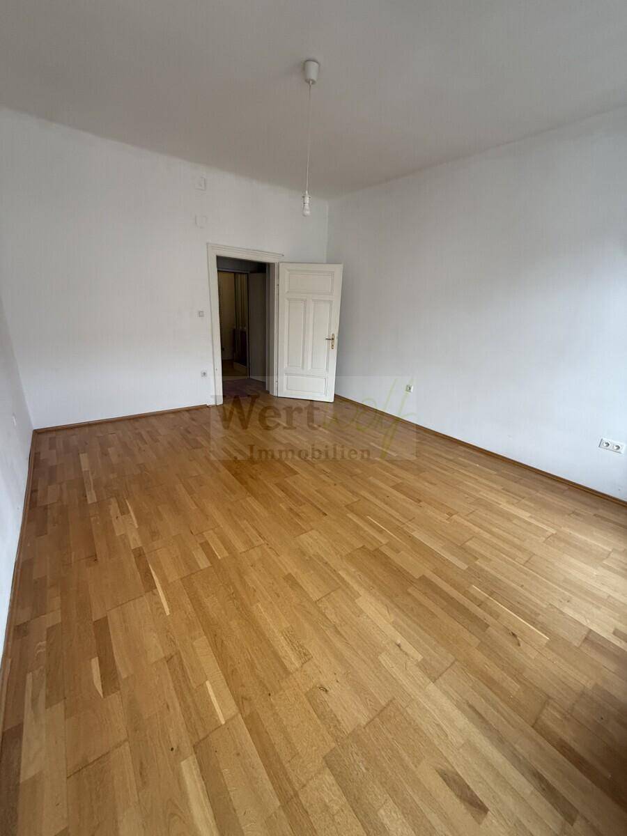 Helles Zimmer mit Parkettboden und einer Tür, die zu einem weiteren Bereich der Wohnung führt.