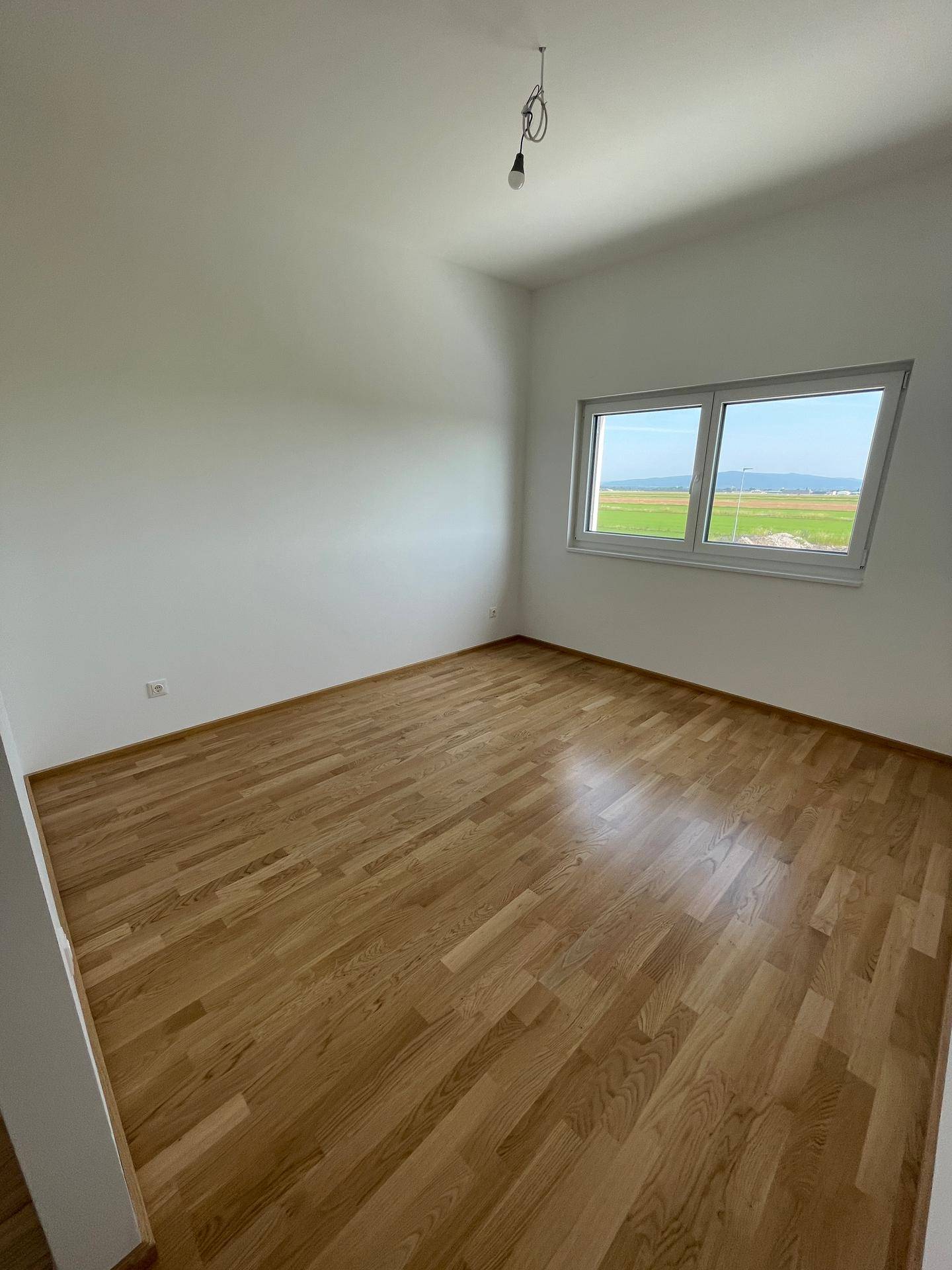 Geräumiges Schlafzimmer mit Holzboden und großem Fenster, das viel Tageslicht hereinlässt.