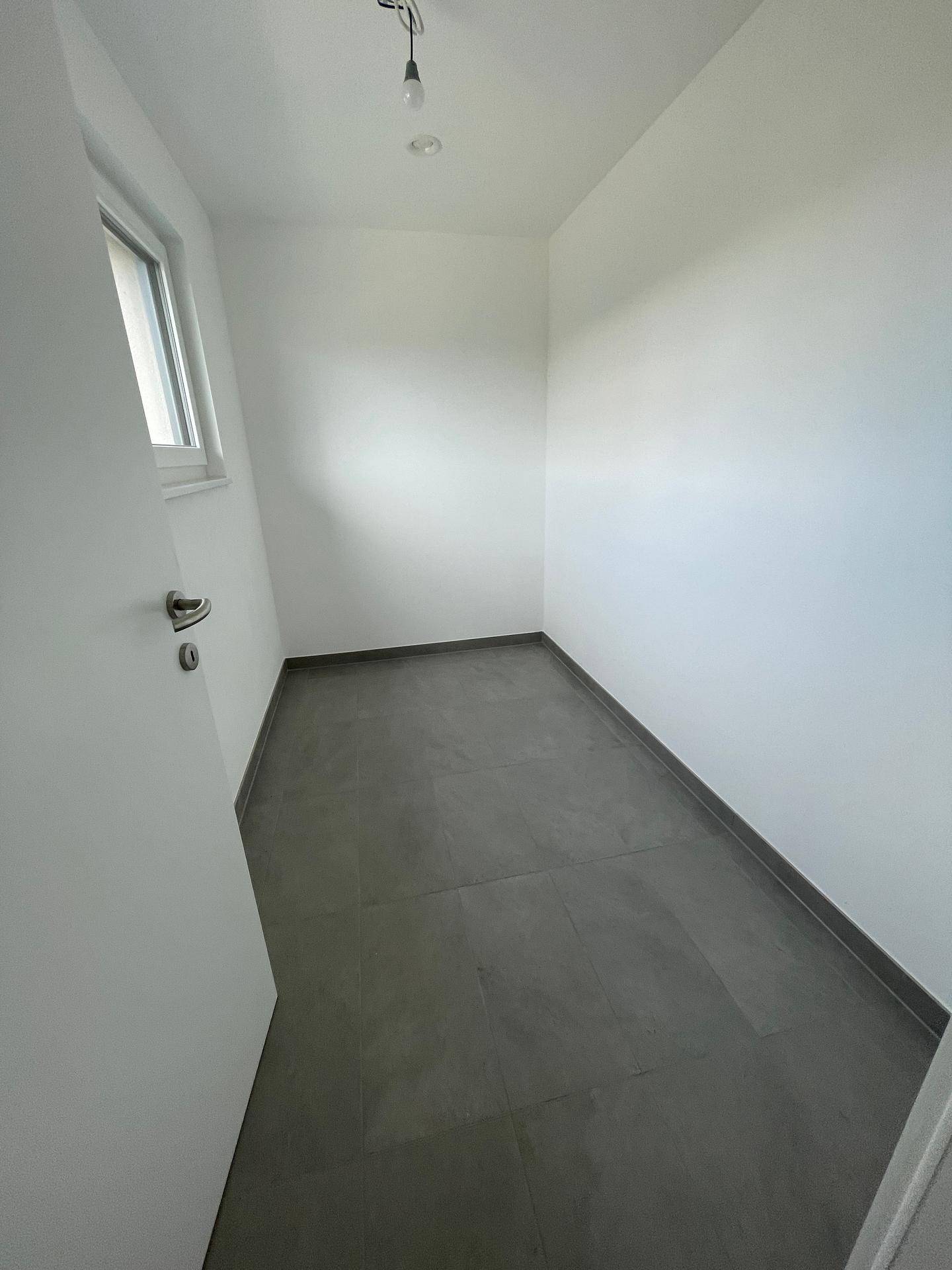 Praktischer Abstellraum mit Fenster und pflegeleichten grauen Fliesen, ideal für zusätzlichen Stauraum.
