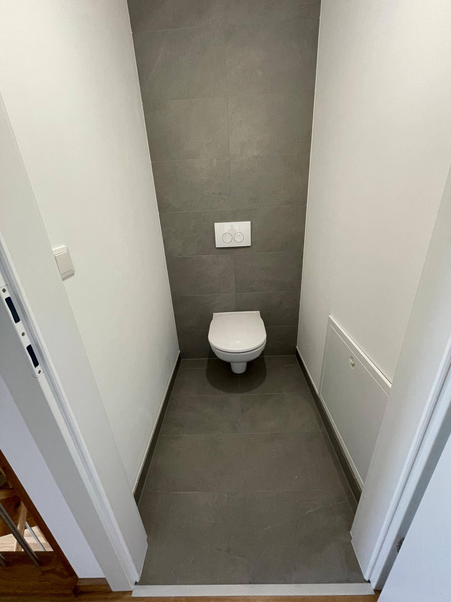 Kompaktes Gäste-WC mit grauen Fliesen und wandhängendem WC, ideal für Besucher.
