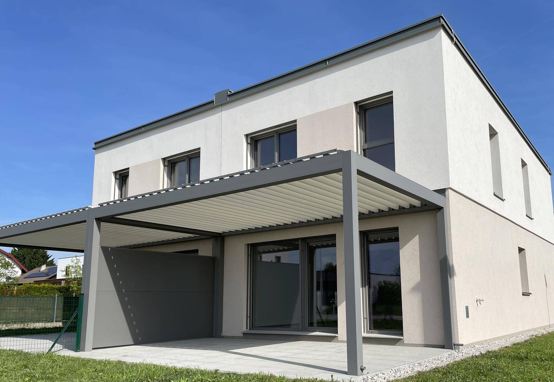 Rückseite eines modernen Hauses mit großer Terrasse und einer stilvollen Pergola für Schatten.