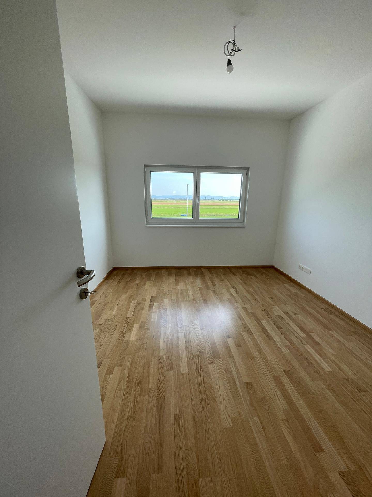 Ruhiges Schlafzimmer mit Holzboden und Fenster, das einen weiten Blick ins Grüne ermöglicht.
