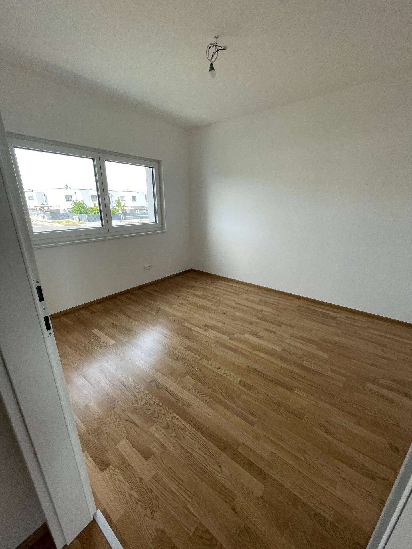 Helles Schlafzimmer mit Holzboden und Fenster, das einen Blick auf die umliegenden Gebäude bietet.