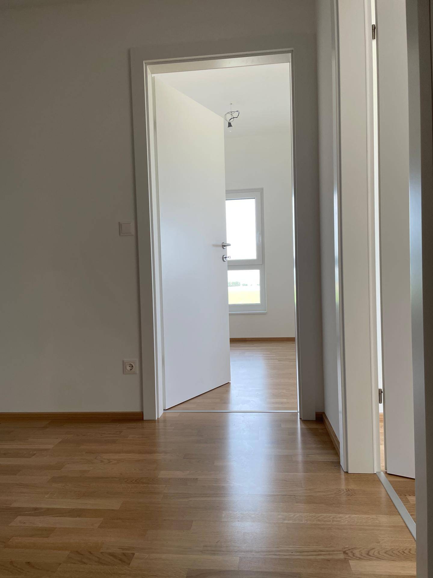 Offene Tür zu einem weiteren hellen Raum mit Holzboden, der vielseitig genutzt werden kann.
