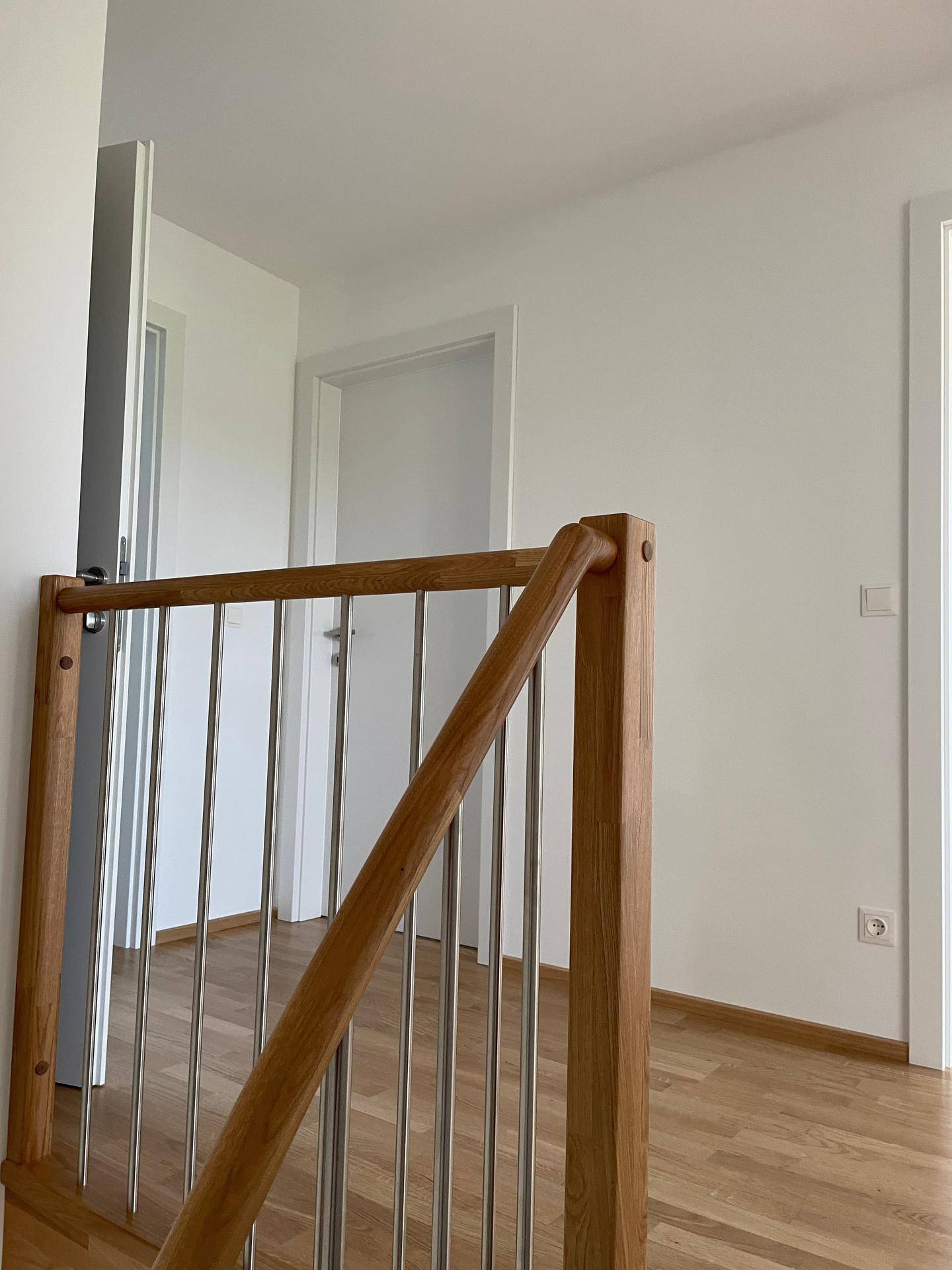 Detailansicht einer modernen Holztreppe mit Edelstahlgeländer in einem hellen Flurbereich.