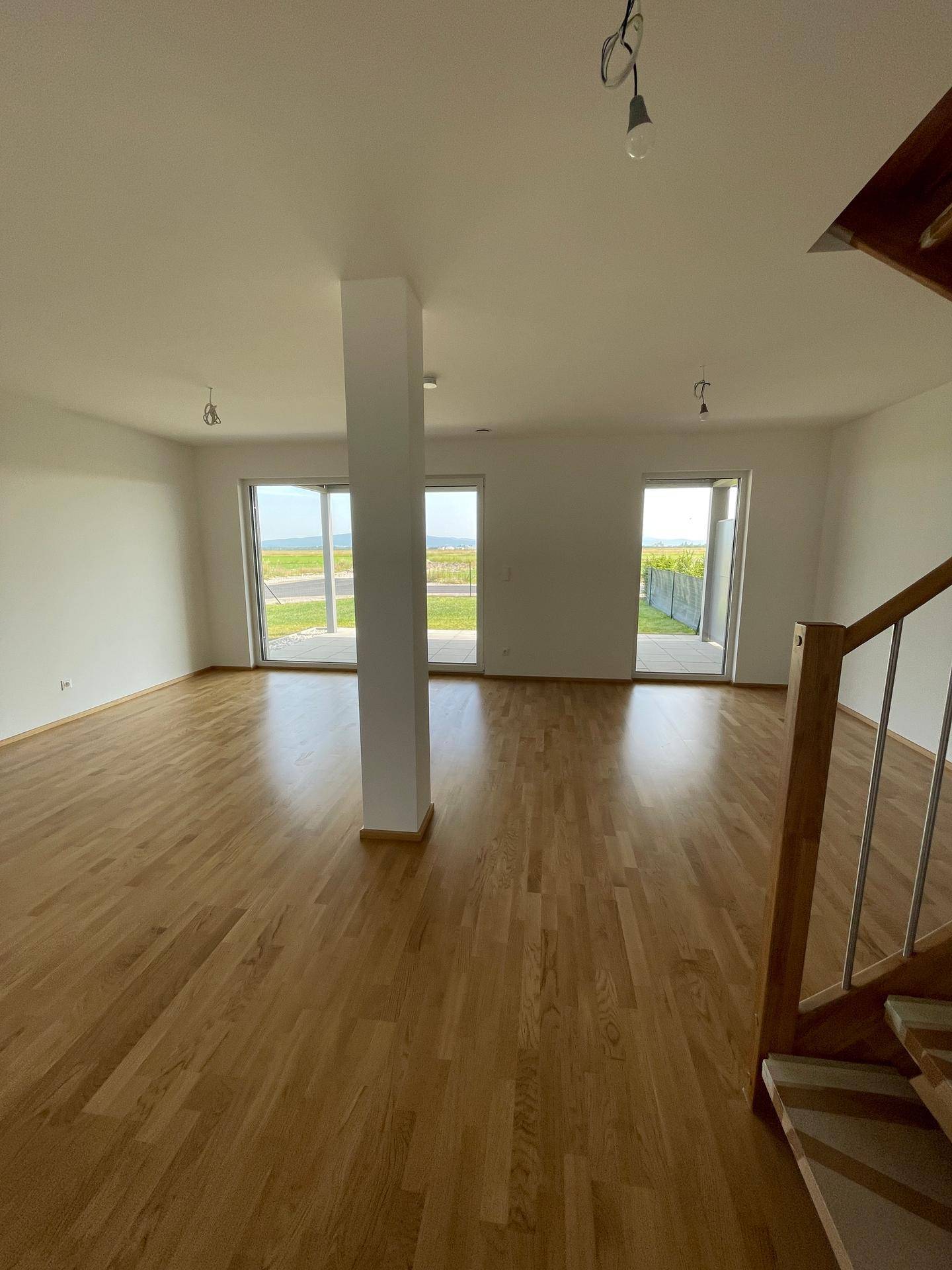 Geräumiger Wohnbereich mit Holzboden und großen Glasfronten, die Zugang zum Außenbereich bieten.