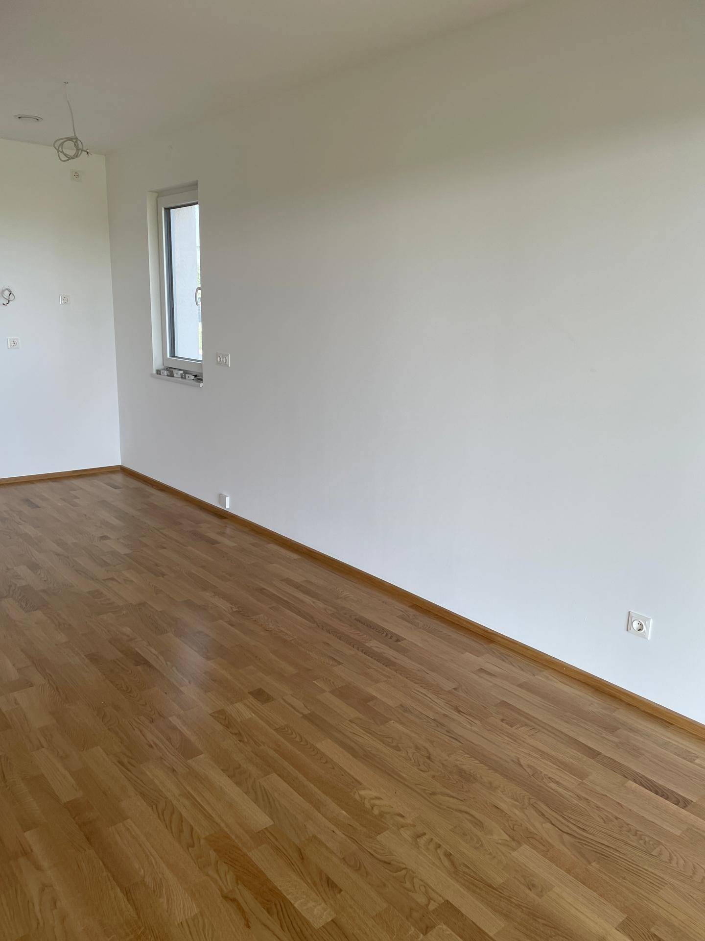 Lichtdurchfluteter Raum mit Holzboden und einem Fenster, ideal für Wohn- oder Essbereich.