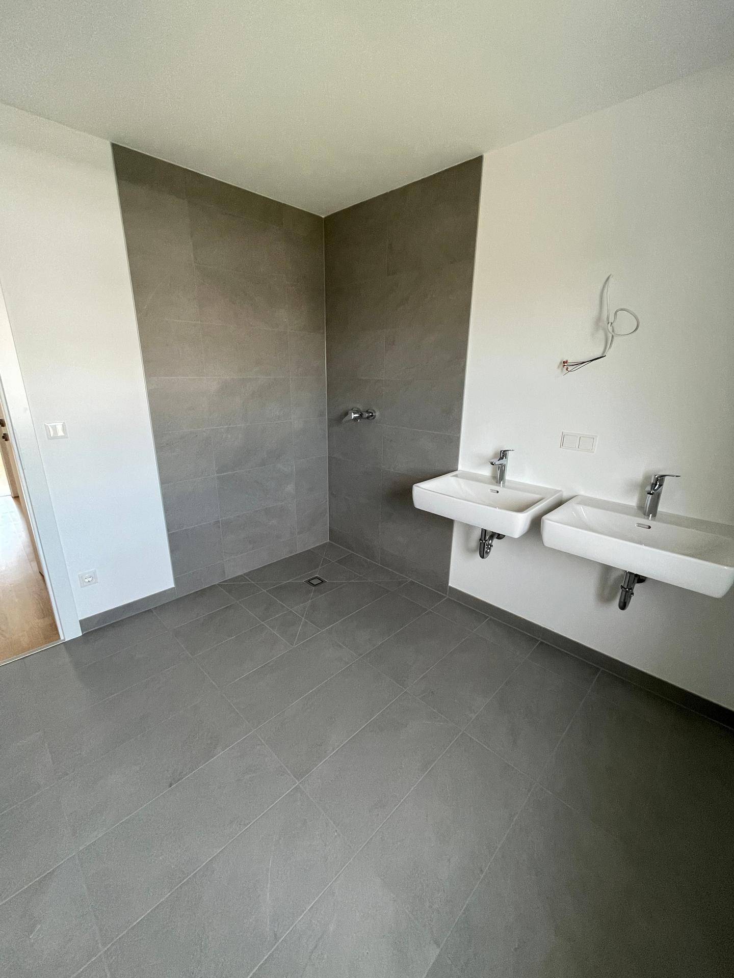 Modernes Badezimmer mit Doppelwaschbecken, geräumiger begehbarer Dusche und eleganten grauen Fliesen.