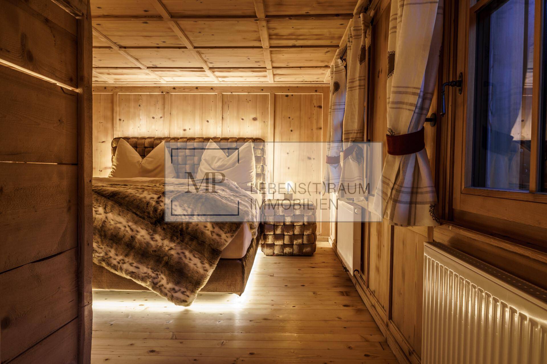 Gemütliches Schlafzimmer im alpinen Stil mit Holzwänden, Holzdecke und einem großen Bett mit Fellüberwurf.