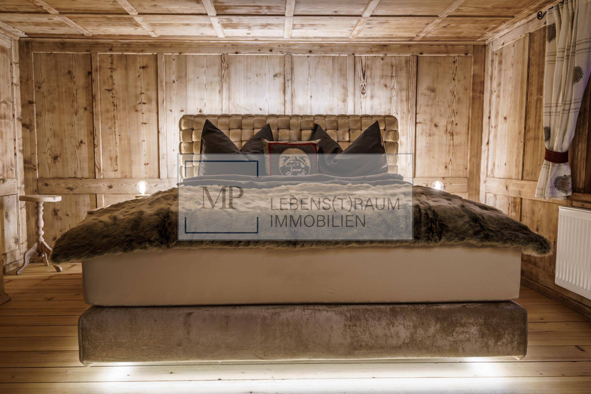Gemütliches Schlafzimmer im alpinen Stil mit Holzwänden, Holzdecke und einem großen Bett mit Fellüberwurf.