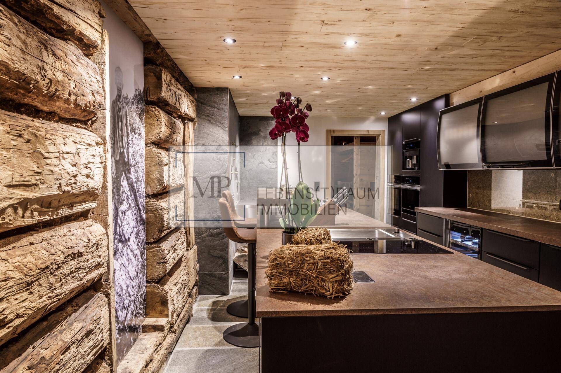 Moderne Küche mit dunklen Schränken, Steinarbeitsplatten, Kücheninsel mit Barhockern und einer Holzwand.