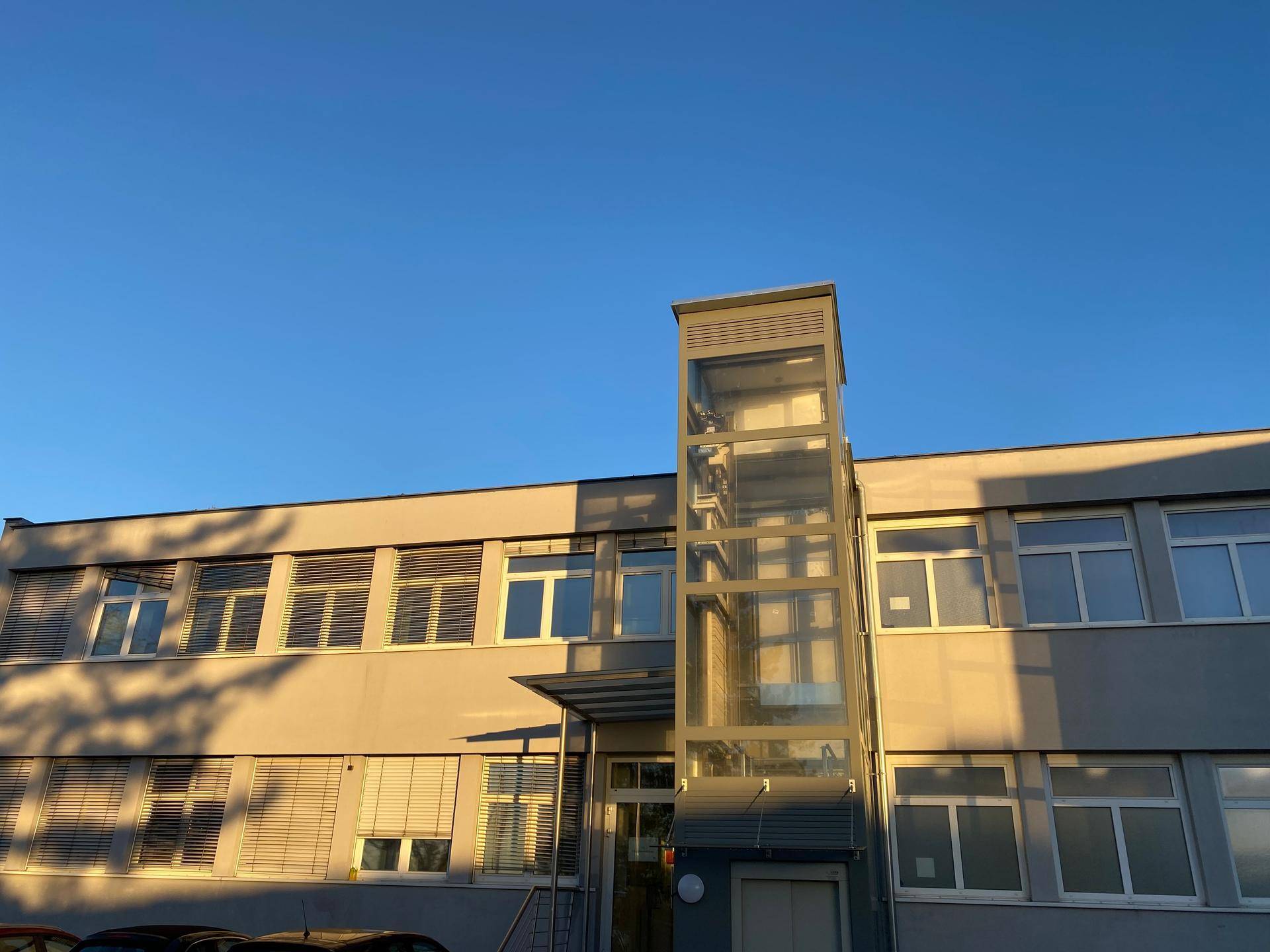 Nahaufnahme des modernen Glasaufzugs und der Fassade eines Bürogebäudes bei Sonnenuntergang.