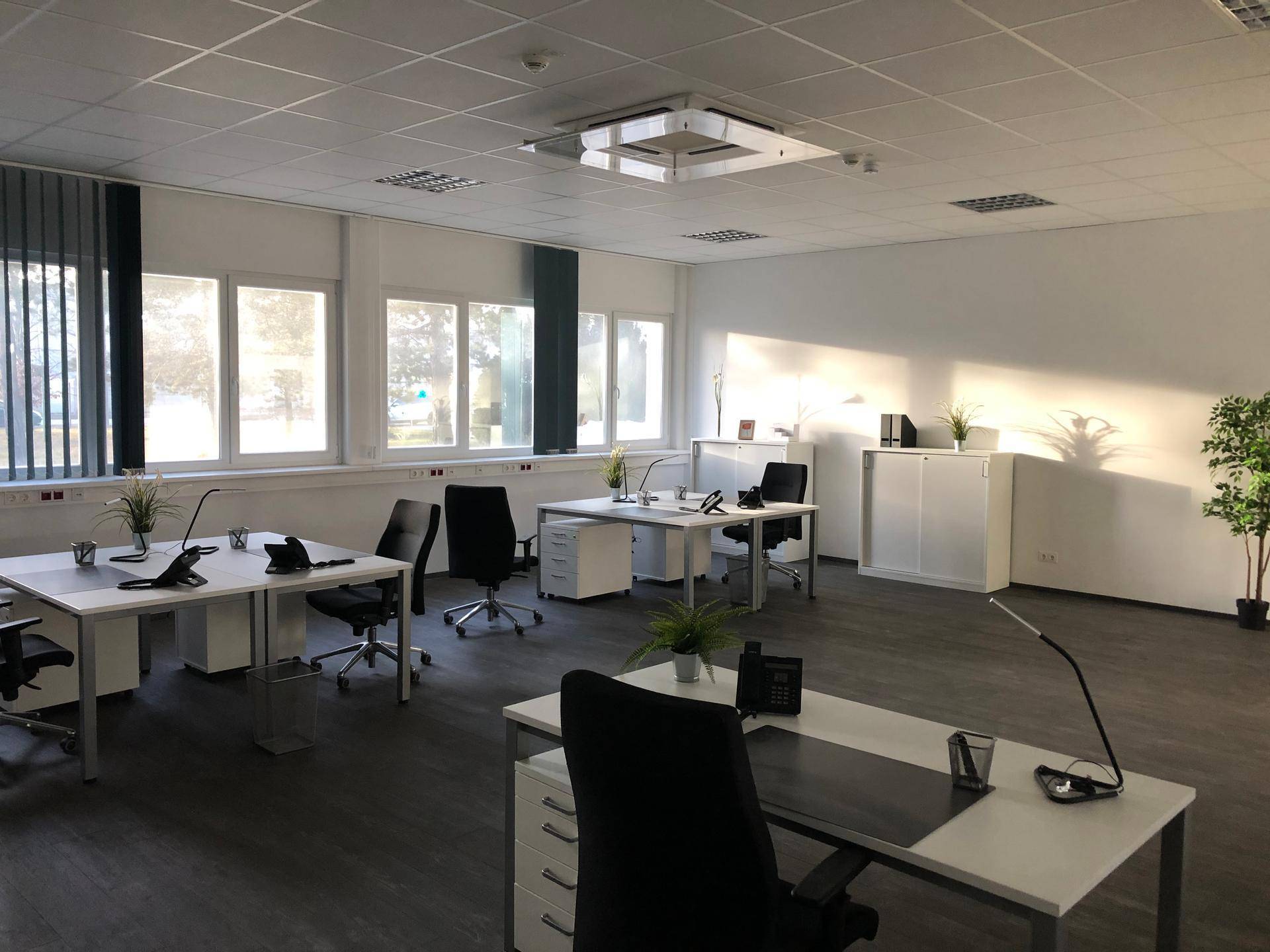 Modernes Büro mit dunklem Boden, mehreren Arbeitsplätzen und viel Tageslicht durch große Fenster.