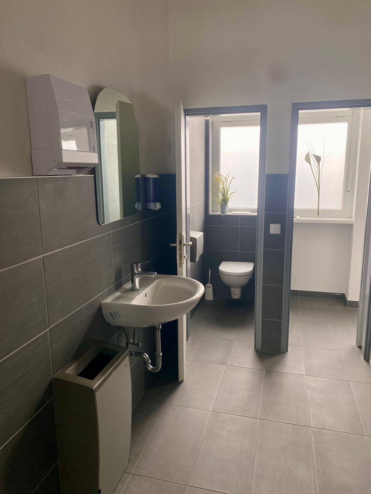 Moderne Toilette mit Waschbecken, Spiegel und dunklen Fliesen an Wänden und Boden.