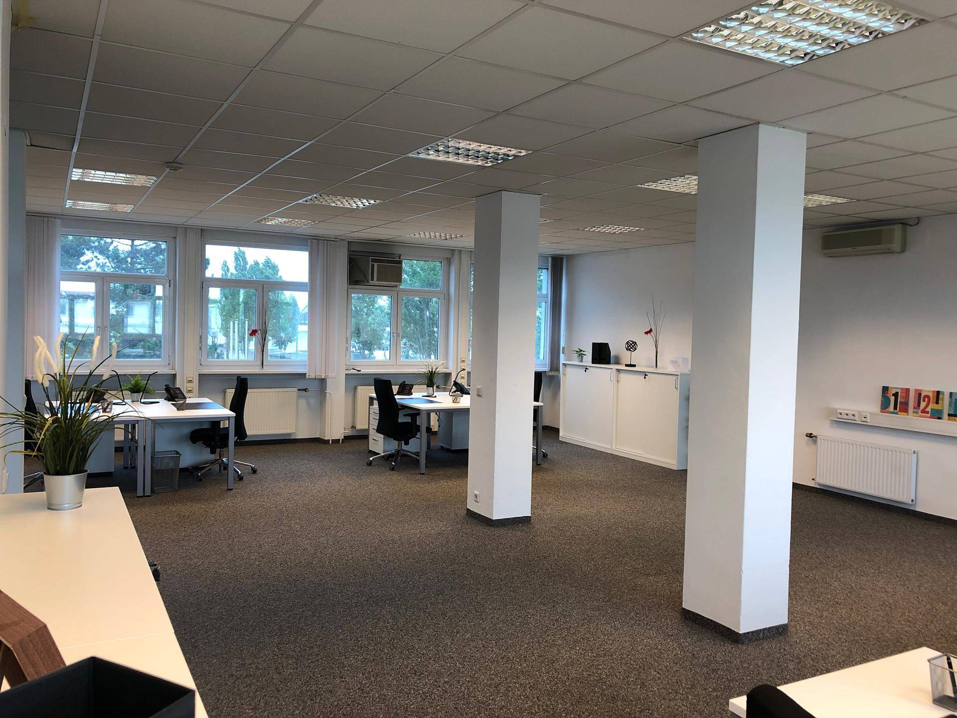 Geräumiger Büroraum mit mehreren Arbeitsplätzen, Säulen und Fenstern mit Ausblick.