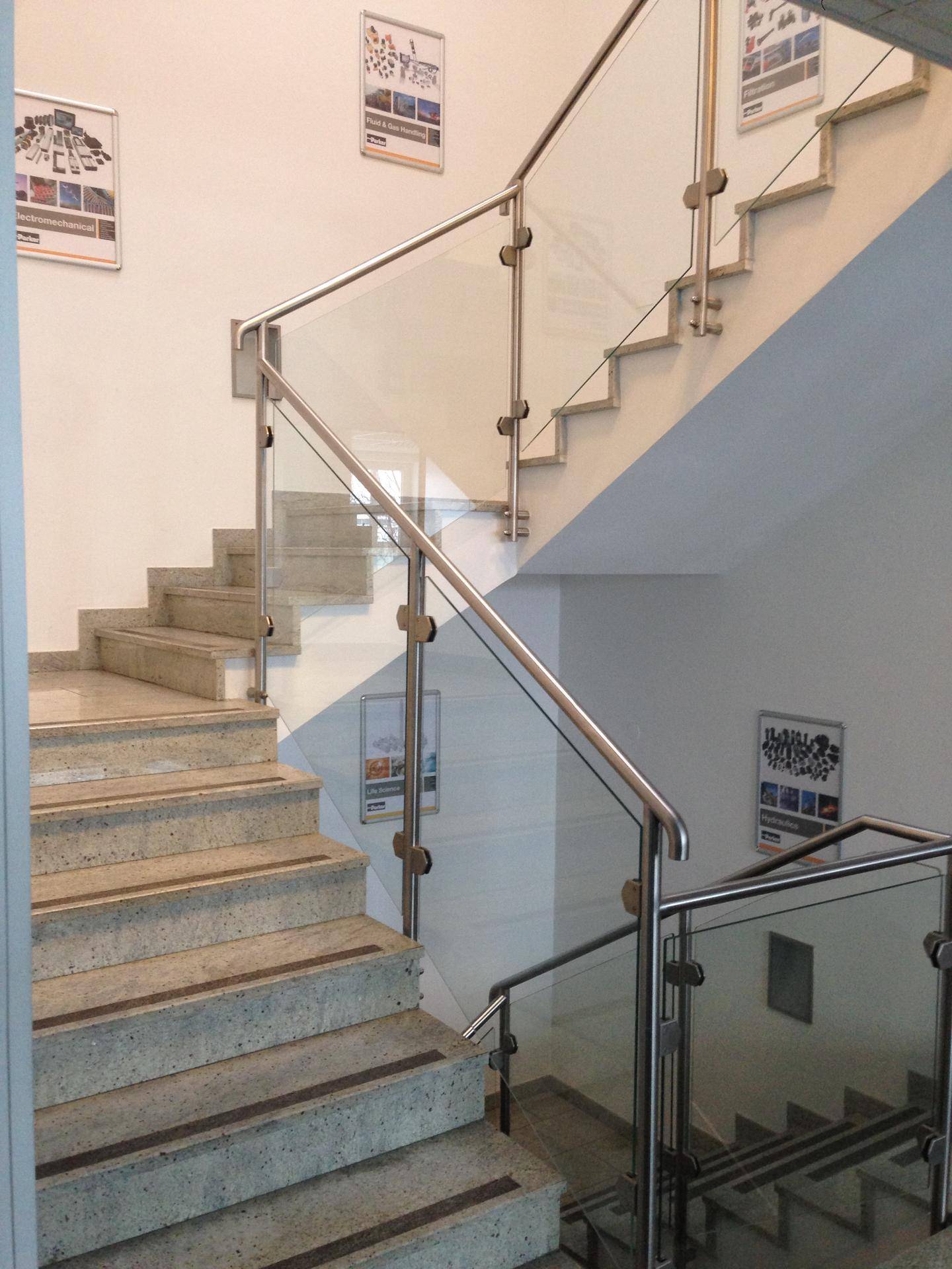 Modernes Treppenhaus mit Steinstufen, Glasgeländer und Edelstahlhandläufen.