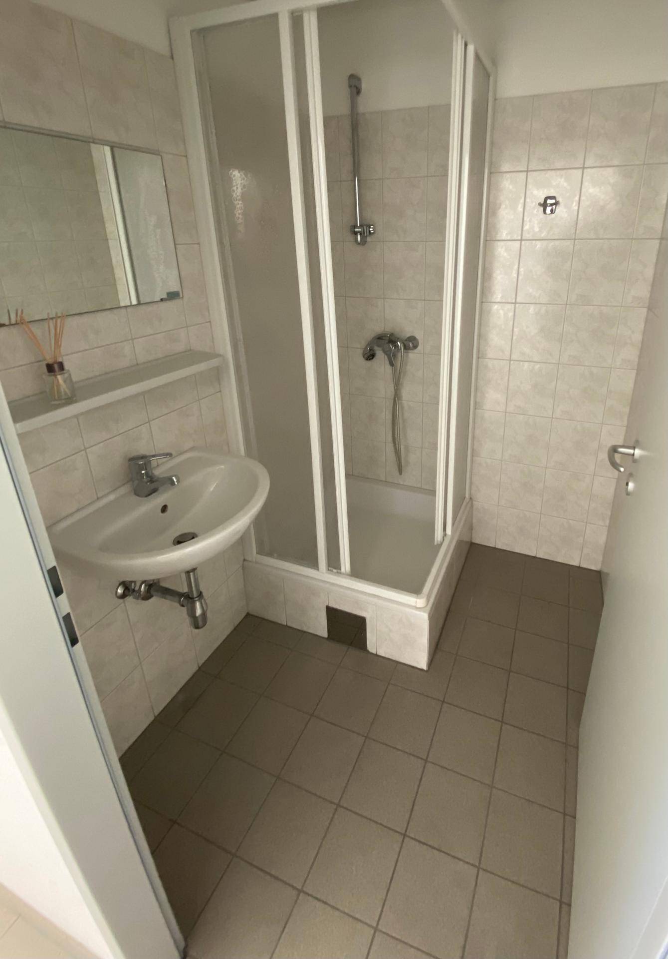 Kleines Badezimmer mit Duschkabine, Waschbecken und hellen Fliesen.