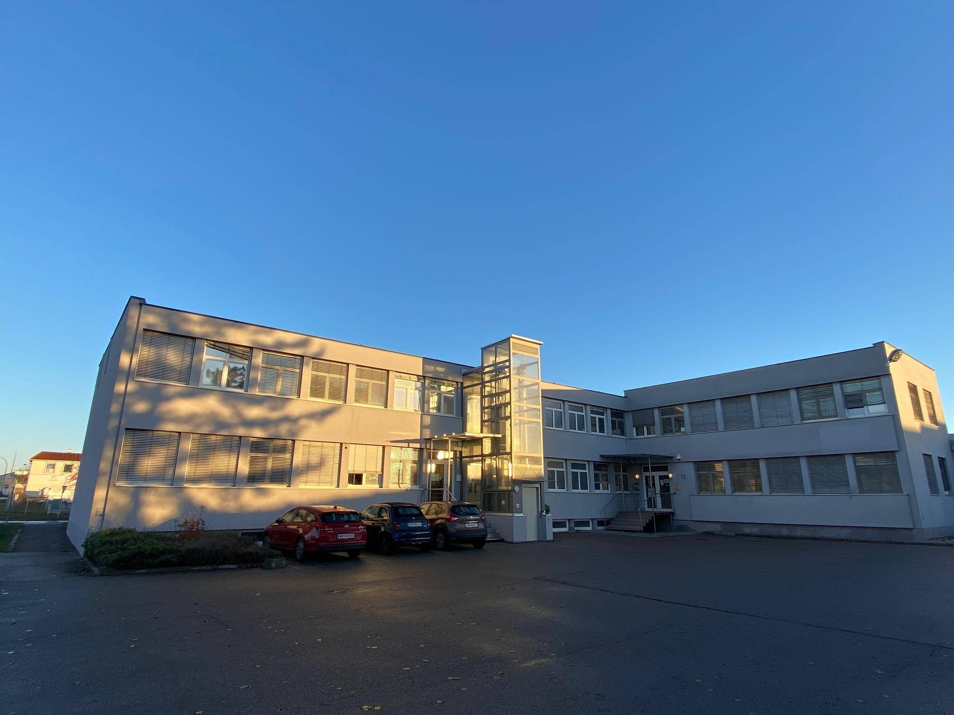 Gesamtansicht des modernen Bürokomplexes mit Parkplätzen und klarem Himmel.