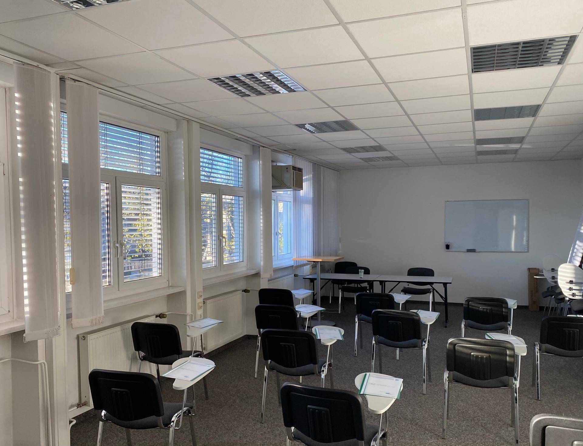 Großer Konferenzraum mit vielen Stühlen, Teppichboden und einer weißen Tafel, ideal für Schulungen.