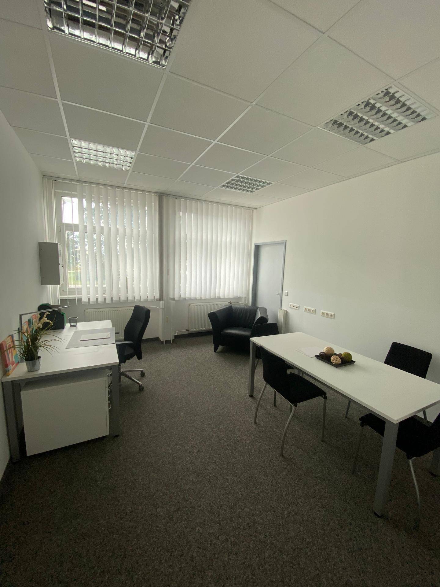 Kleineres Büro oder Besprechungsraum mit Teppichboden, Schreibtisch und Sitzgelegenheiten.