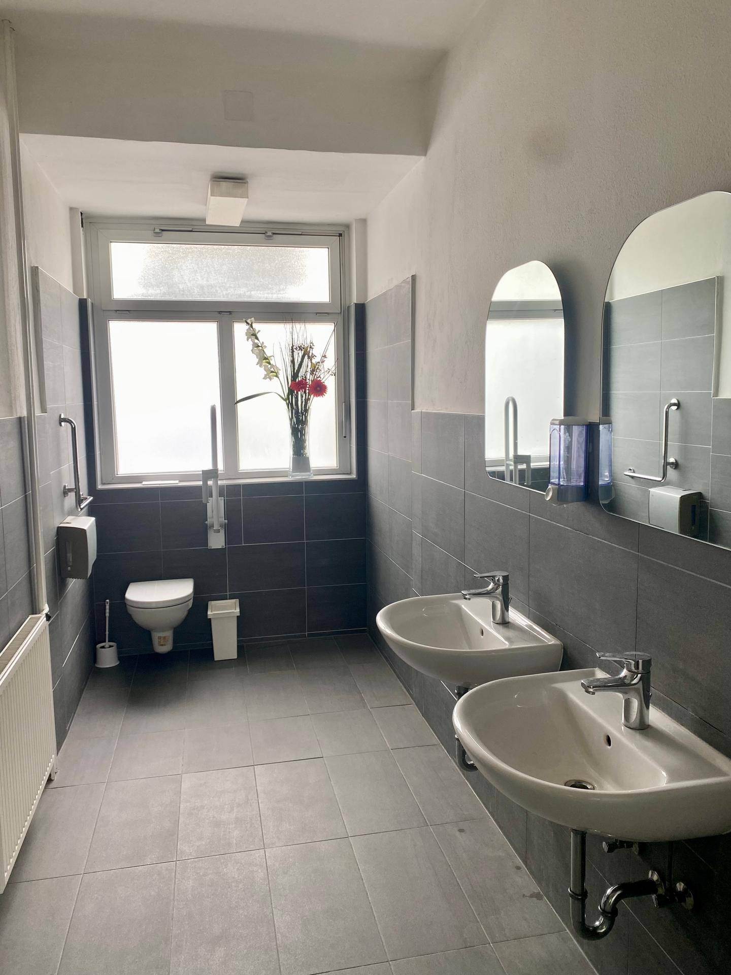 Modernes Badezimmer mit zwei Waschbecken, Wand-WC und großen Fliesen an Wänden und Boden.
