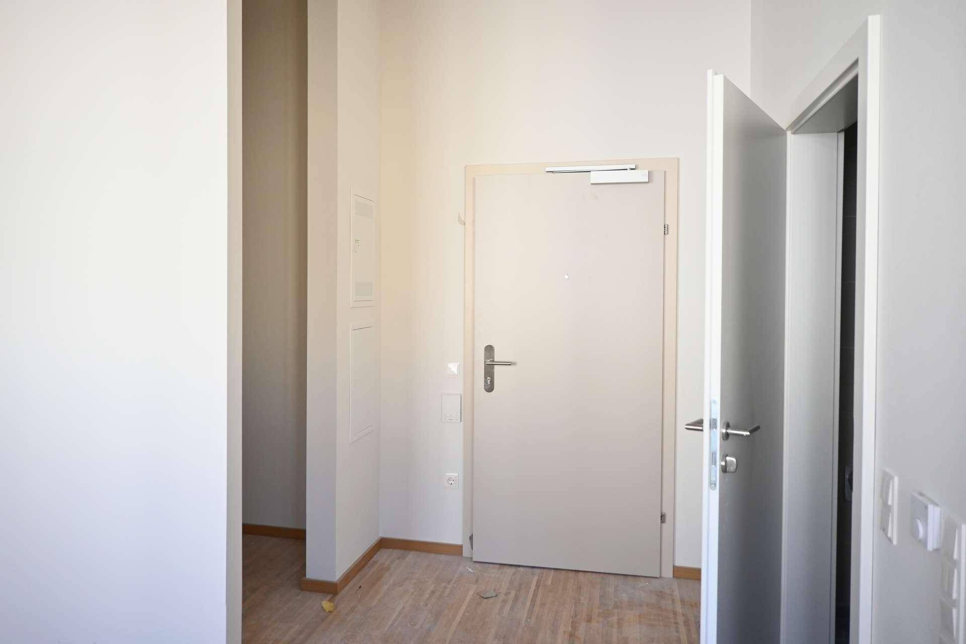 Heller Flur mit zwei Türen und hellem Holzfußboden, der zu weiteren Räumen führt.
