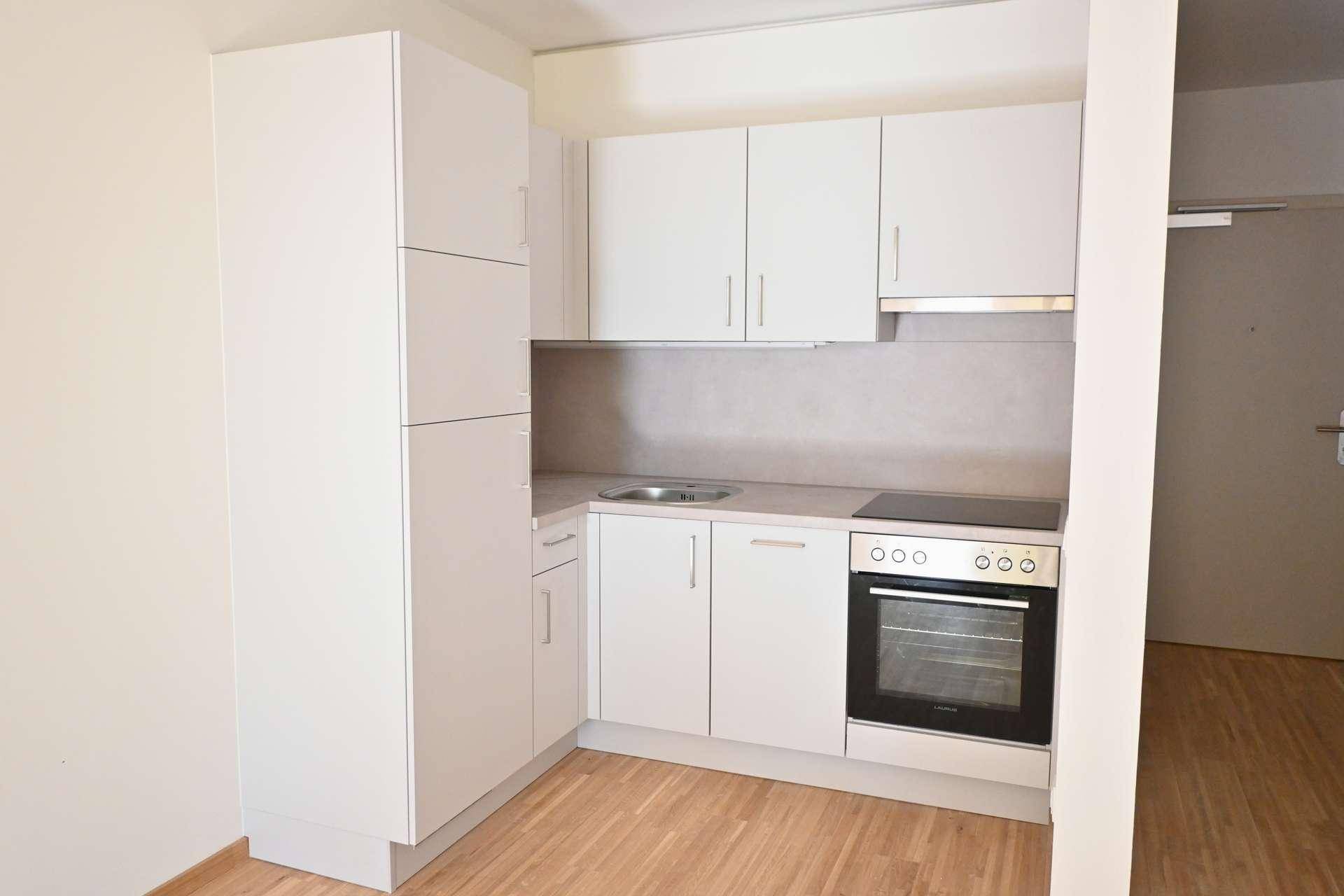 Moderne, kompakte Einbauküche in Weiß mit integrierten Geräten und hellem Holzboden.