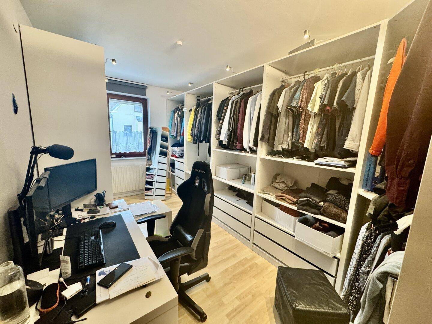 Arbeitszimmer mit integriertem begehbarem Kleiderschrank und Schreibtisch am Fenster.
