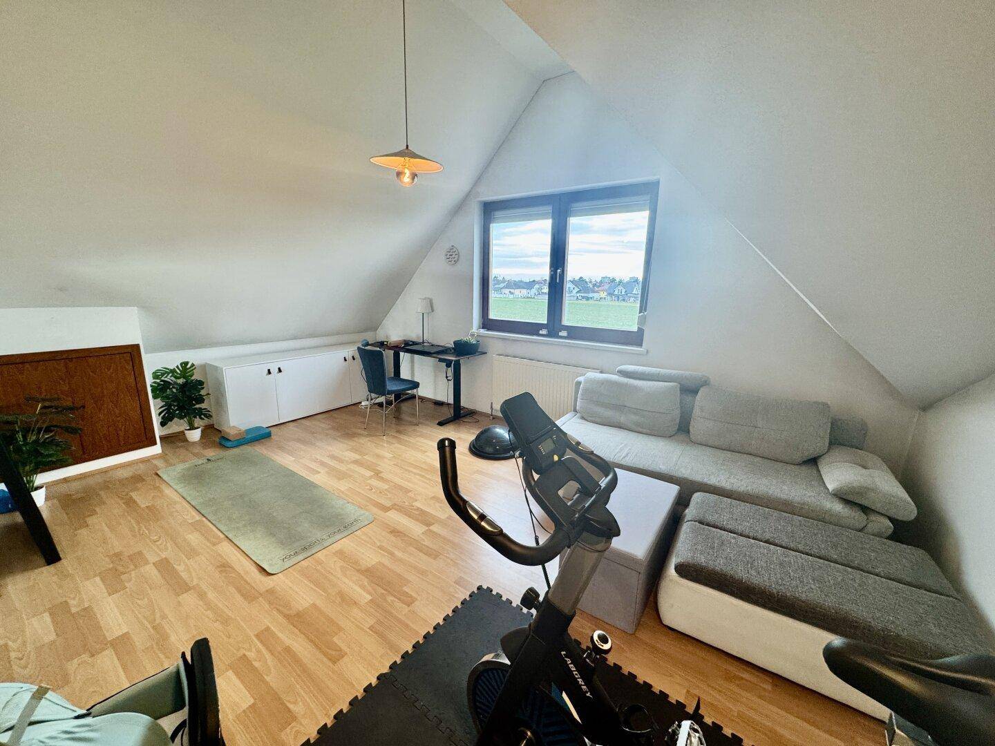 Heller Dachbodenraum mit Schreibtisch, Sofa und Fitnessgeräten unter den Dachschrägen.