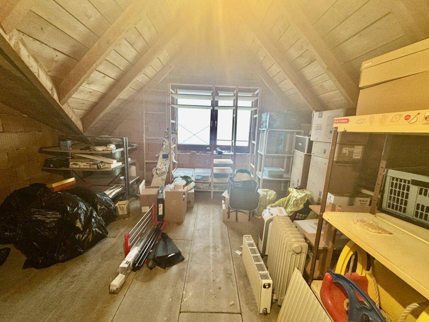 Unausgebauter Dachbodenbereich mit sichtbaren Holzbalken, genutzt als Lagerraum für diverse Gegenstände.