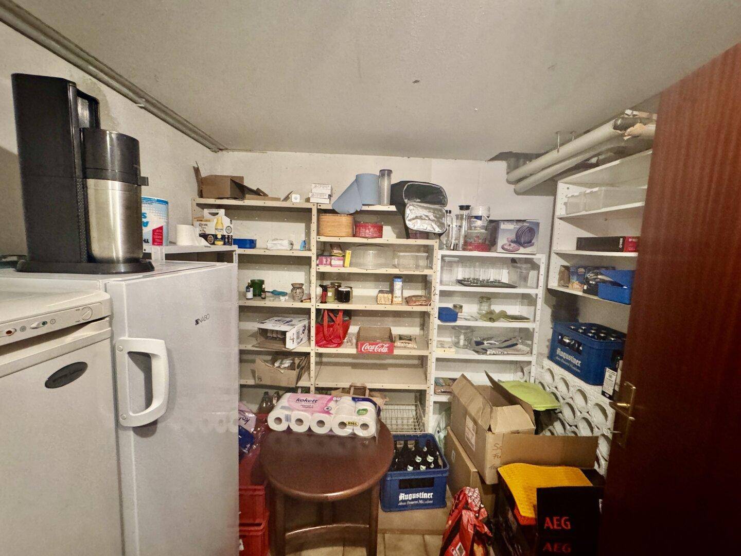 Kellerraum mit Regalen, Kühlschrank und Vorräten, ideal als Lagerfläche.