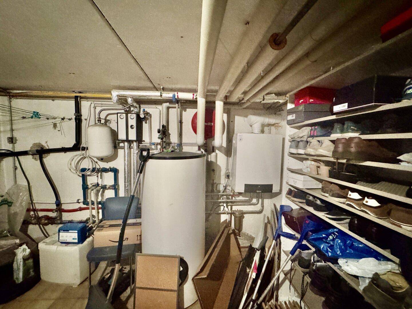Heizungsraum im Keller mit Warmwasserspeicher, Heizungsanlage und Schuhregalen.