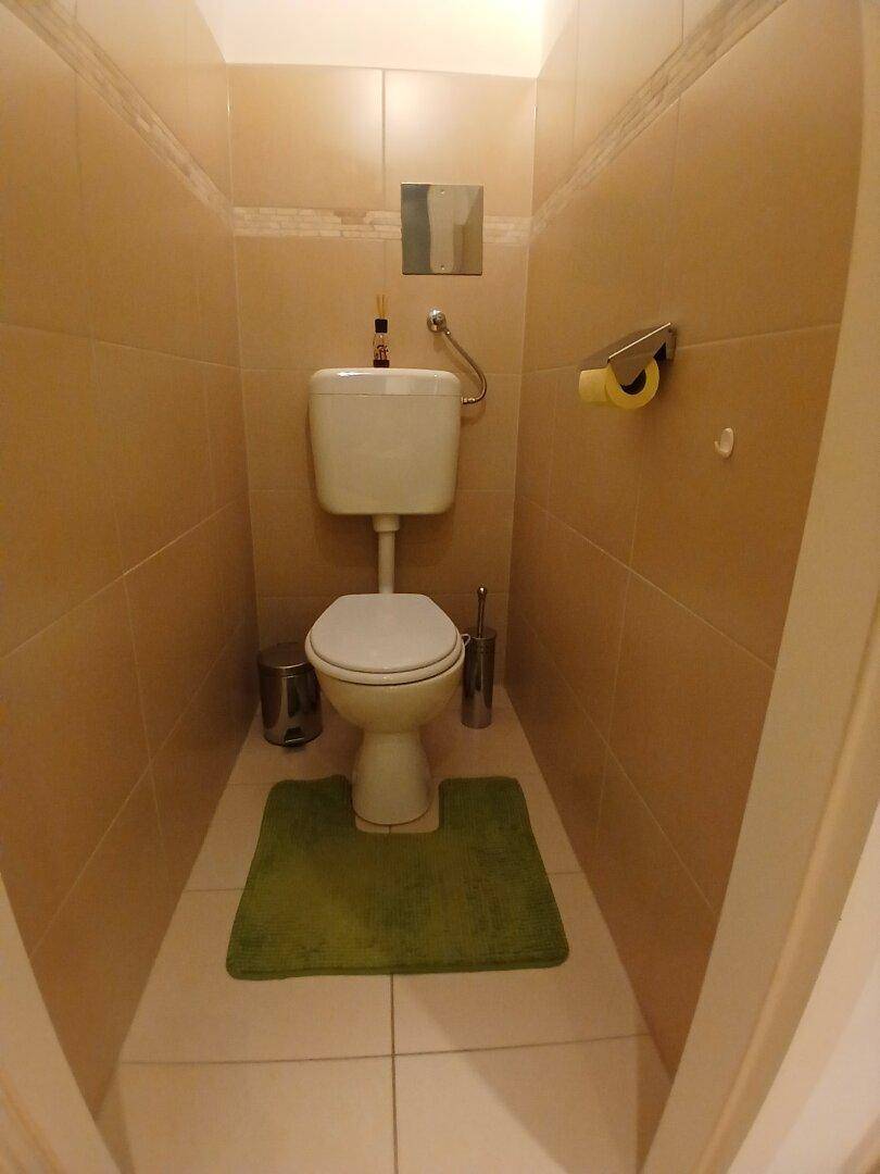 Separates WC mit Toilette und beigefarbenen Fliesen an Wänden und Boden.