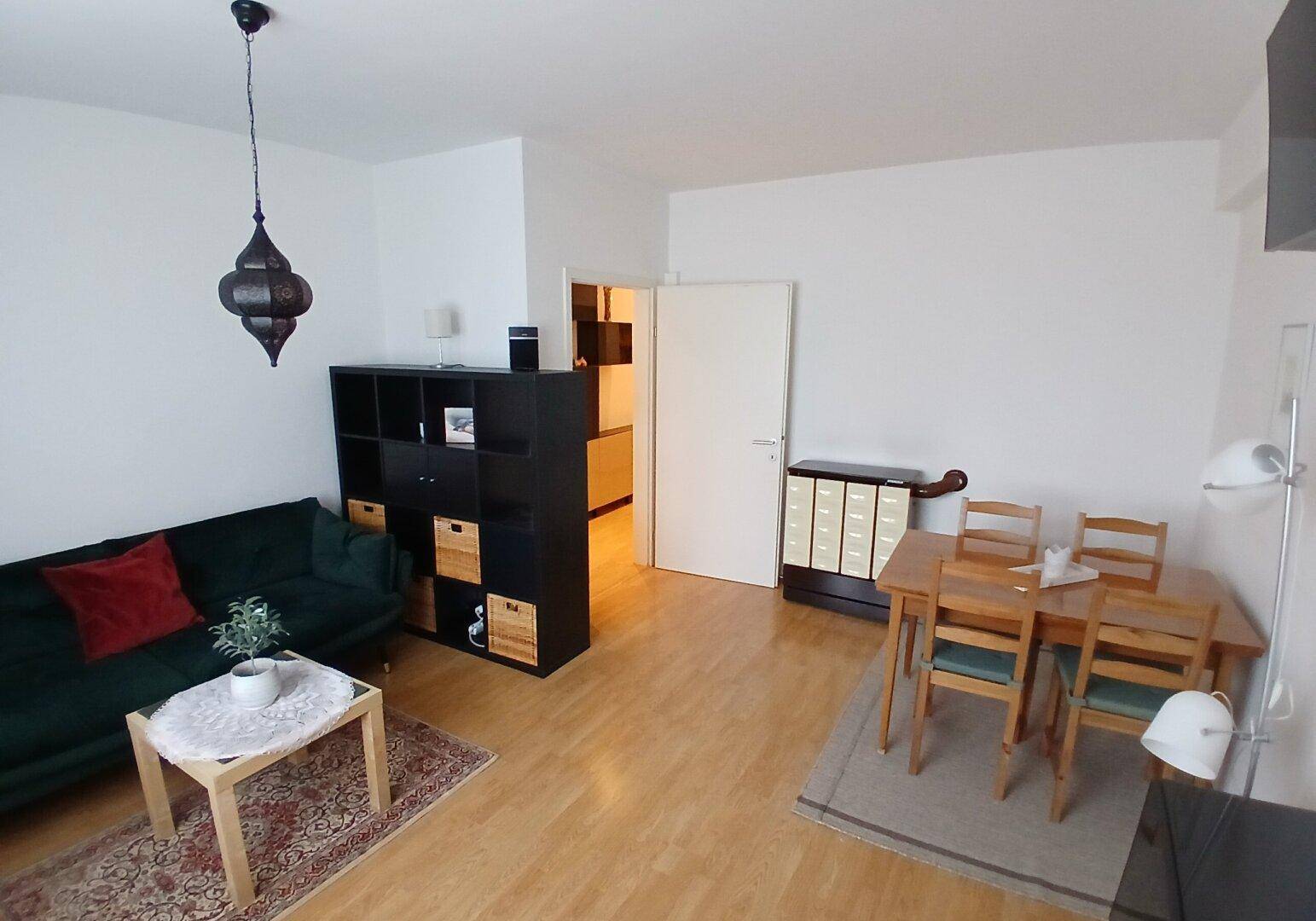 Gemütlicher Wohn-Essbereich mit dunklem Sofa, Esstisch und Holzfußboden, der zum Entspannen einlädt.