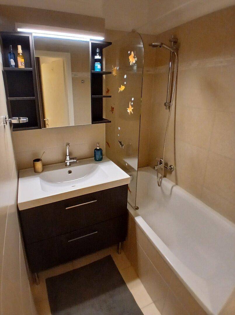 Badezimmer mit Badewanne, Duschvorrichtung, Einzelwaschbecken und Spiegelschrank.