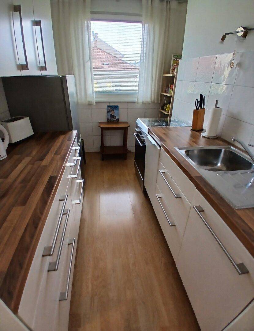 Schmale Küche mit Holz-Arbeitsplatten, weißen Unterschränken und einem Fenster für Tageslicht.