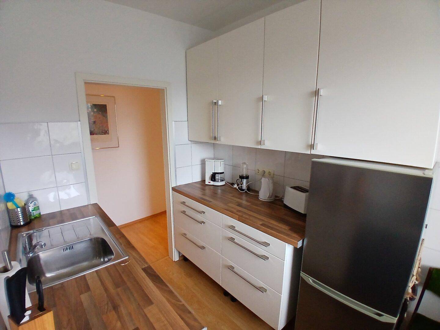 Funktionale Küche mit weißen Hängeschränken, Kühlschrank und Holzarbeitsplatten.