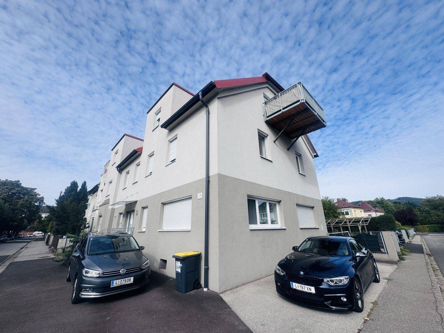 Mehrfamilienhaus mit moderner Fassade und kleinem Balkon unter bewölktem Himmel.