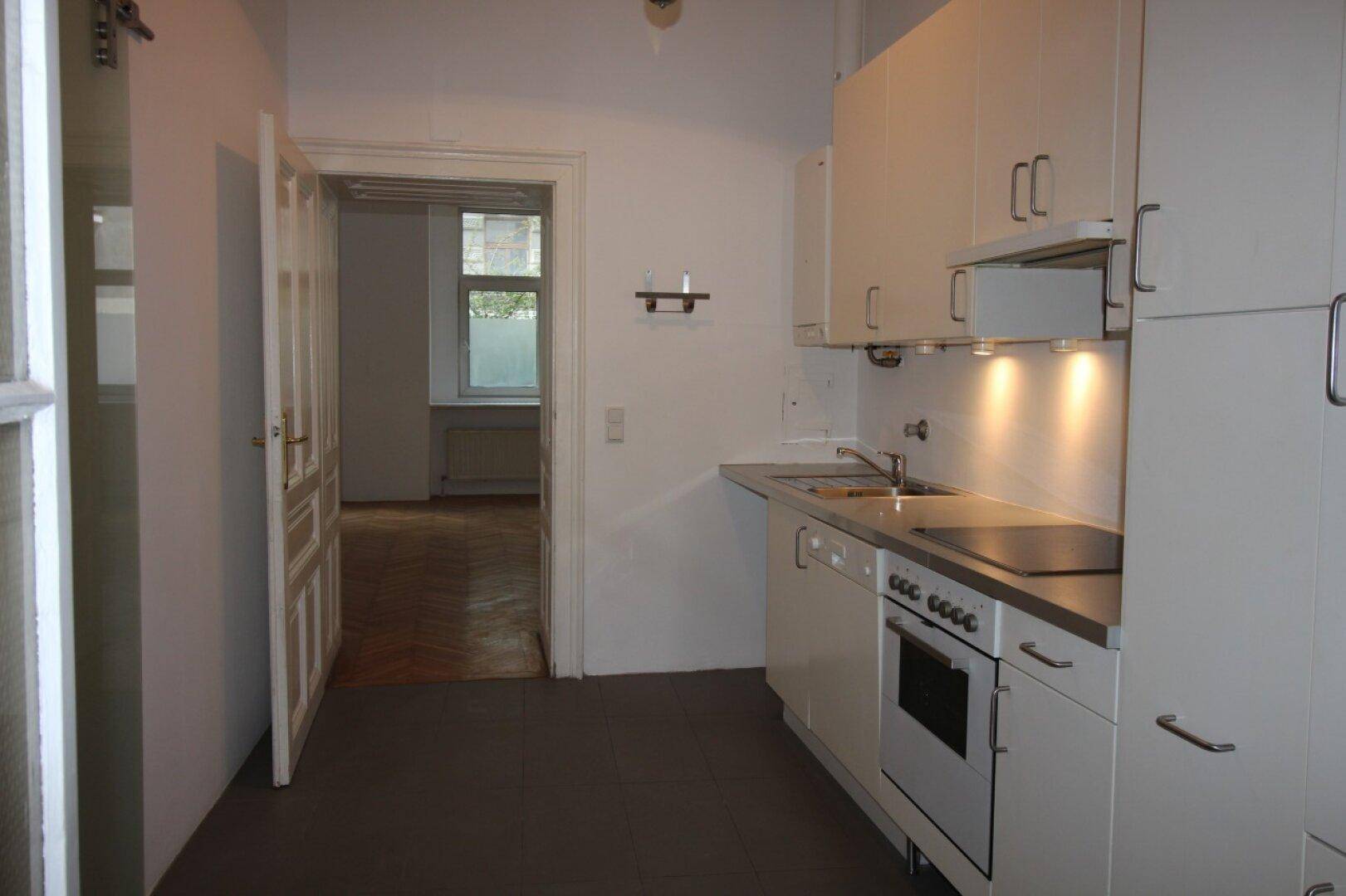 Funktionale Küche mit weißen Schränken und Blick in einen weiteren Raum mit Parkettboden.