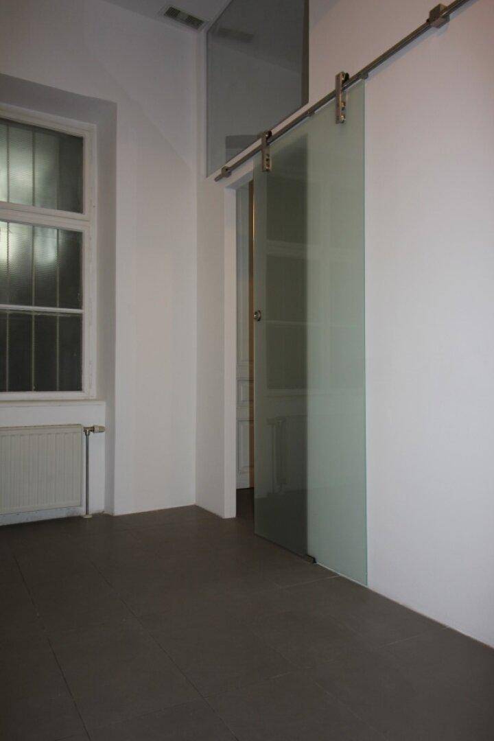 Moderner Raum mit Schiebetür aus Milchglas und Fenster mit Gitter, dunkler Boden.