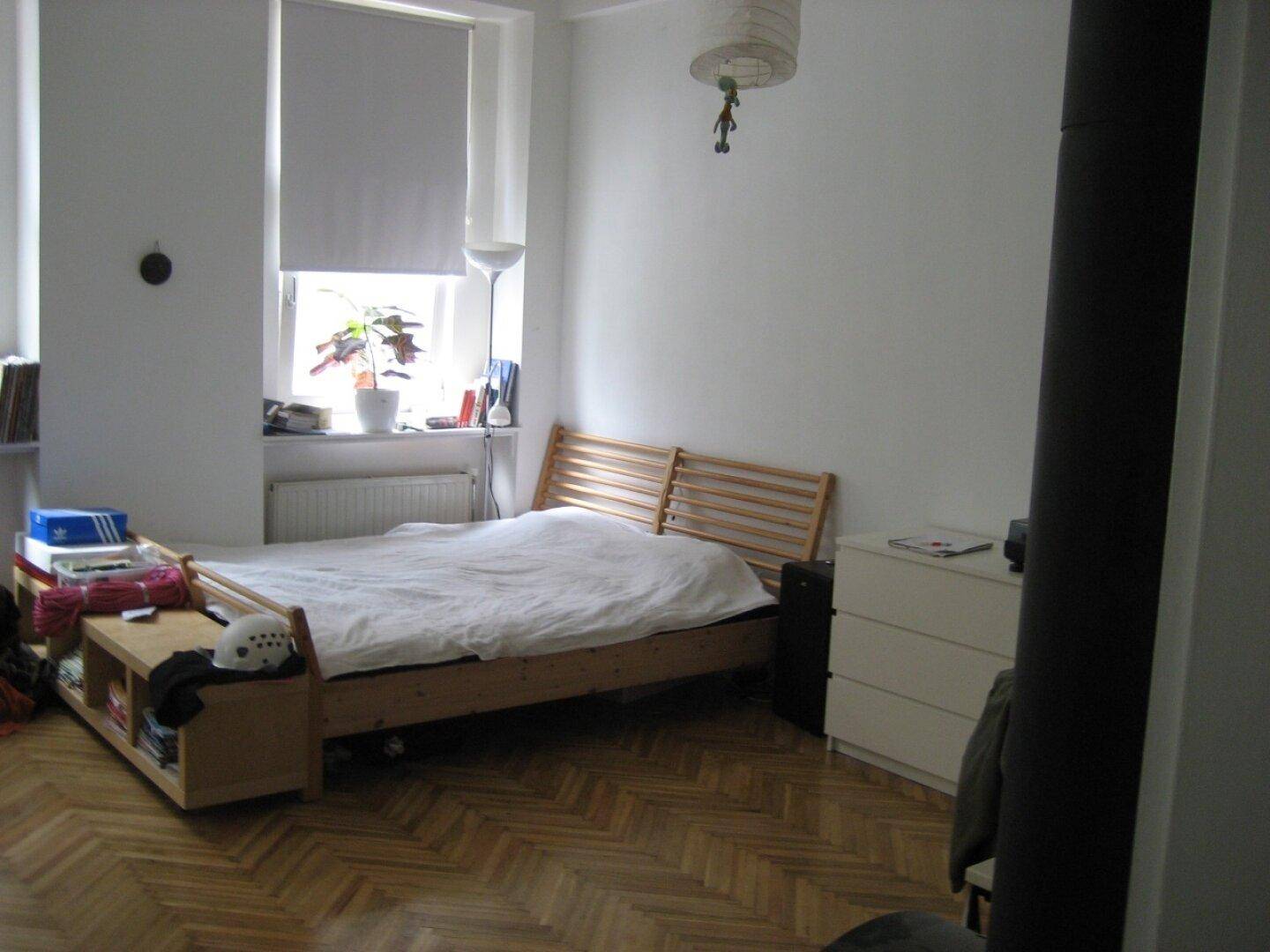 Gemütliches Schlafzimmer mit Holzbett, Fischgrätparkett und einem Fenster mit Rollo.