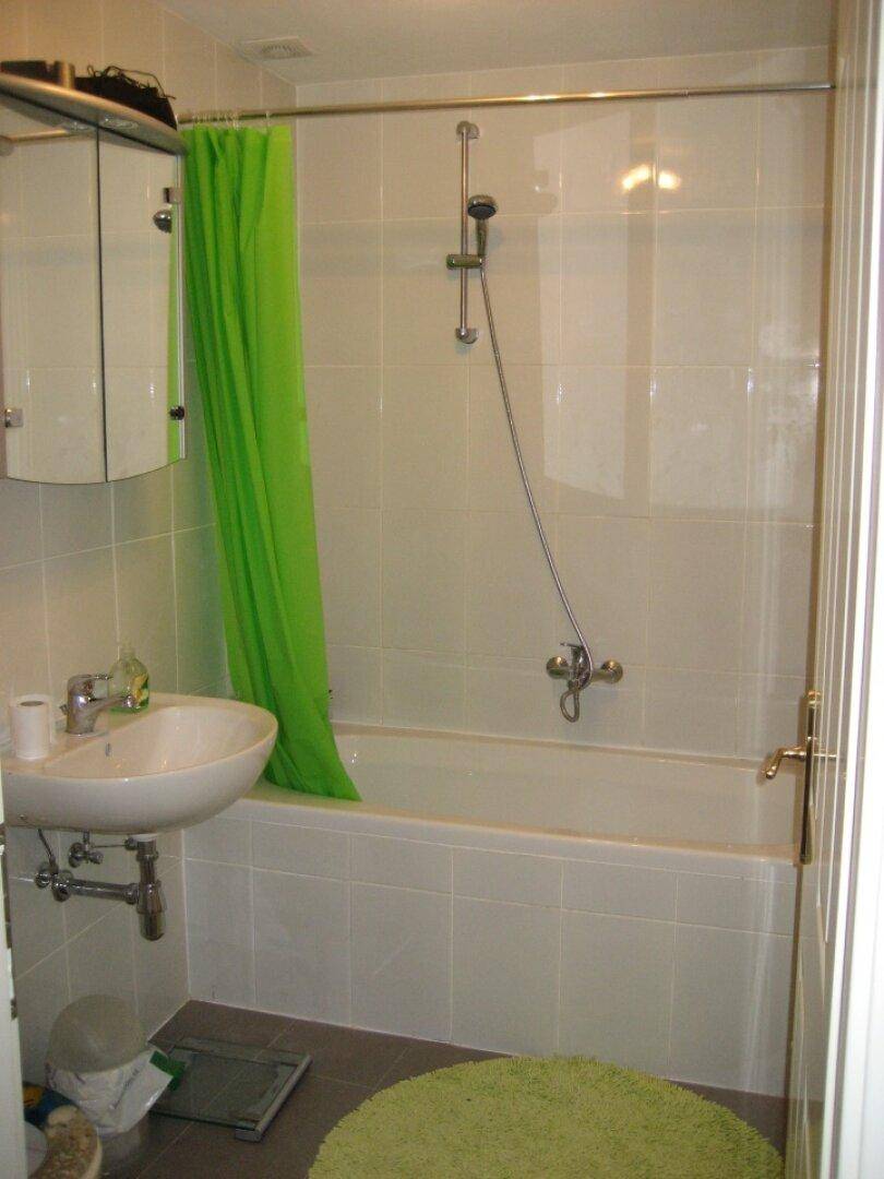 Funktionales Badezimmer mit Badewanne, Duschvorhang und Waschbecken, hell gefliest.