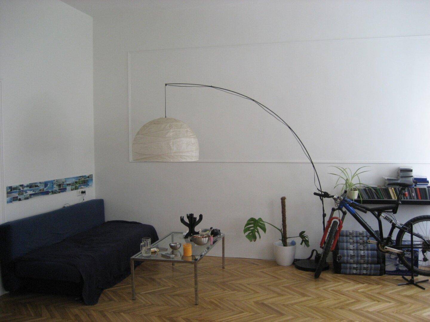 Wohnzimmer mit Sofa, Couchtisch und Fahrrad, beleuchtet von einer modernen Bogenlampe.