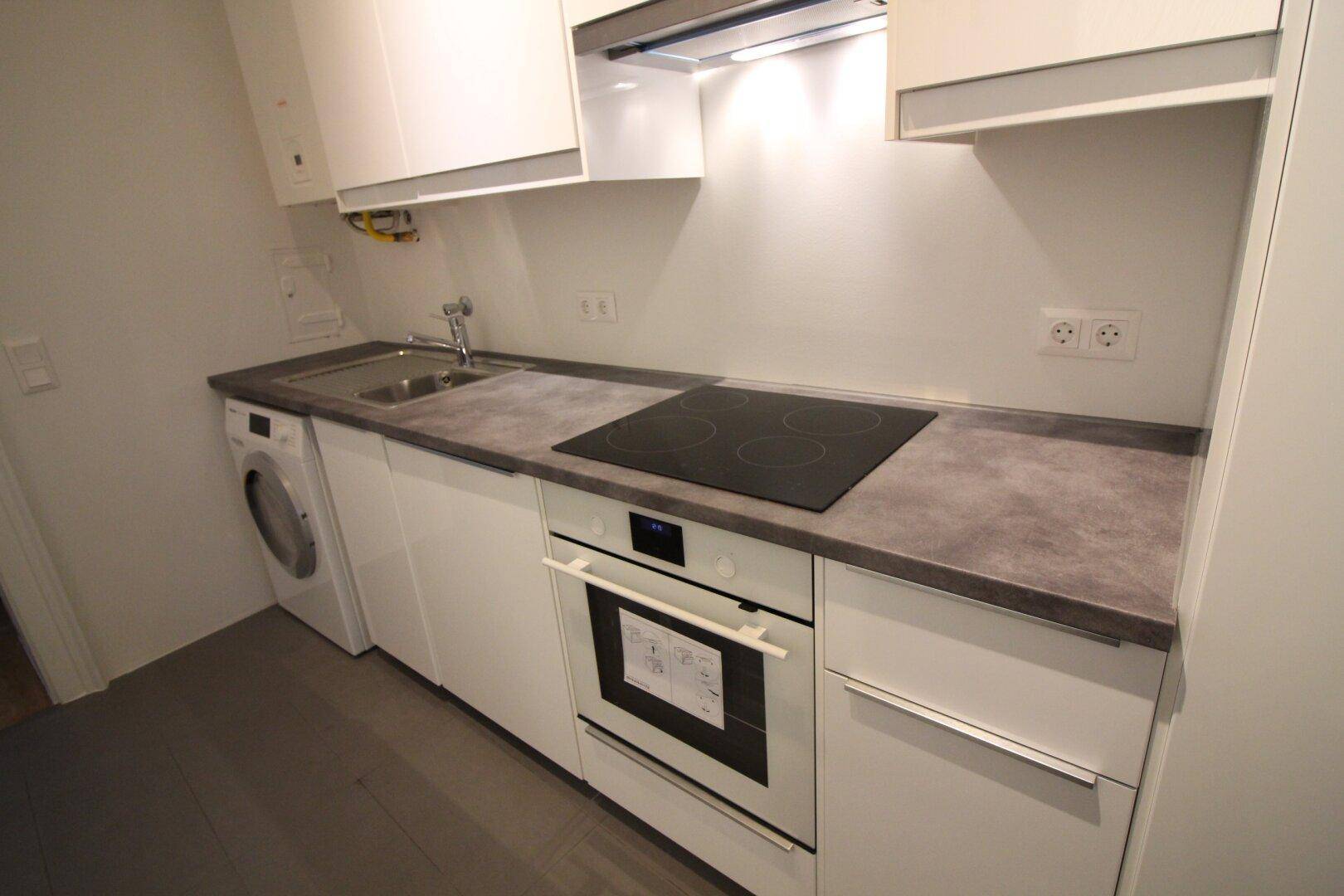 Moderne Einbauküche mit weißen Hochglanzfronten, Induktionskochfeld und integrierter Waschmaschine.