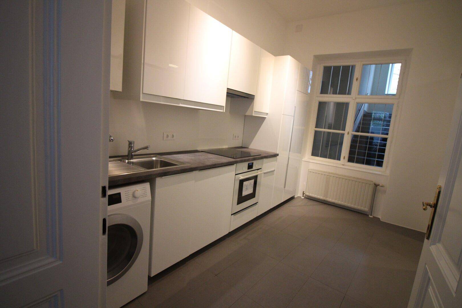 Helle, moderne Küche mit weißen Schränken, Waschmaschine und Fenster mit Jalousien.