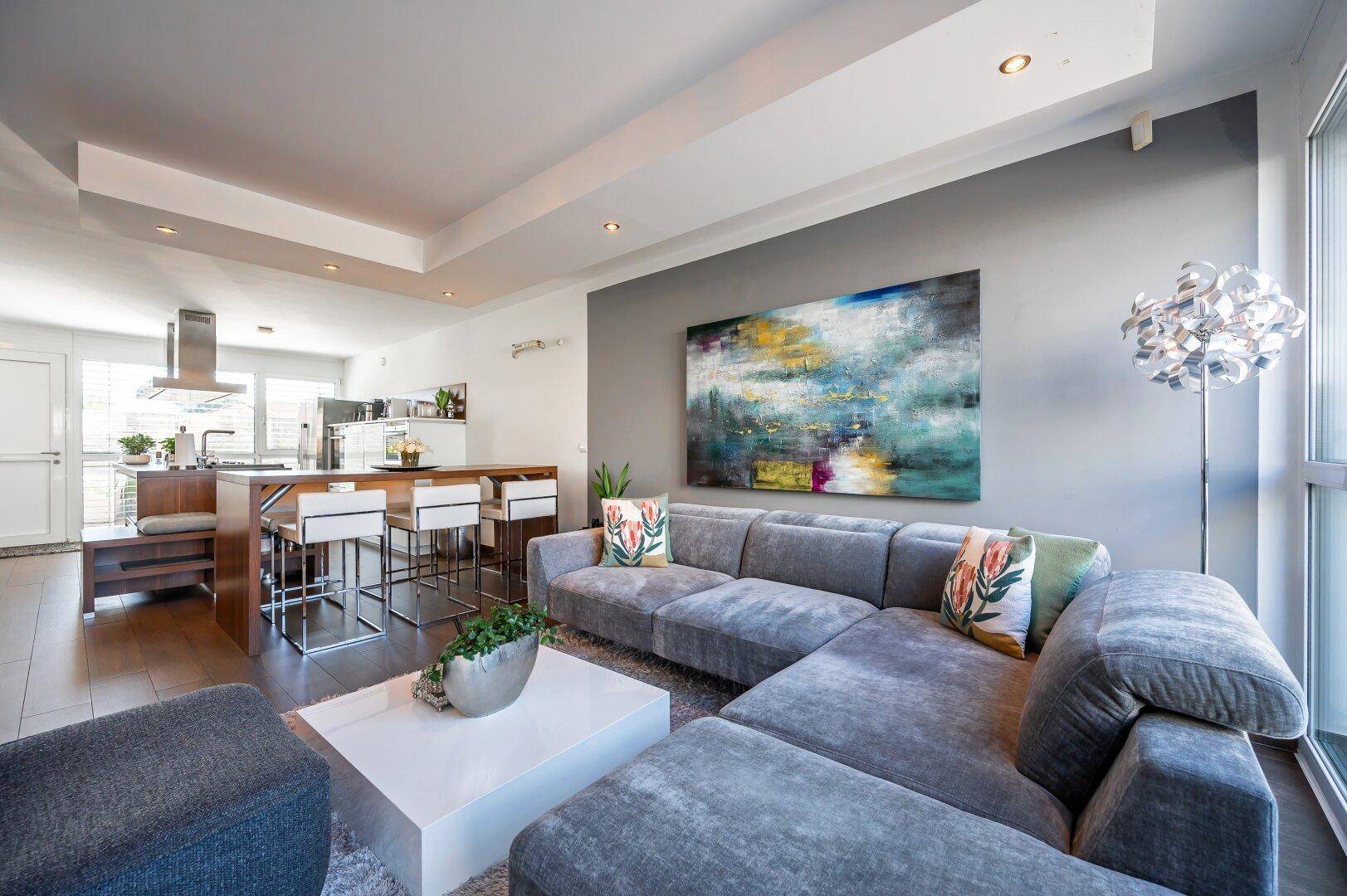 Geräumiges Wohnzimmer mit bequemer Couch, Kunstwerk an der Wand und offener Verbindung zur Küche.