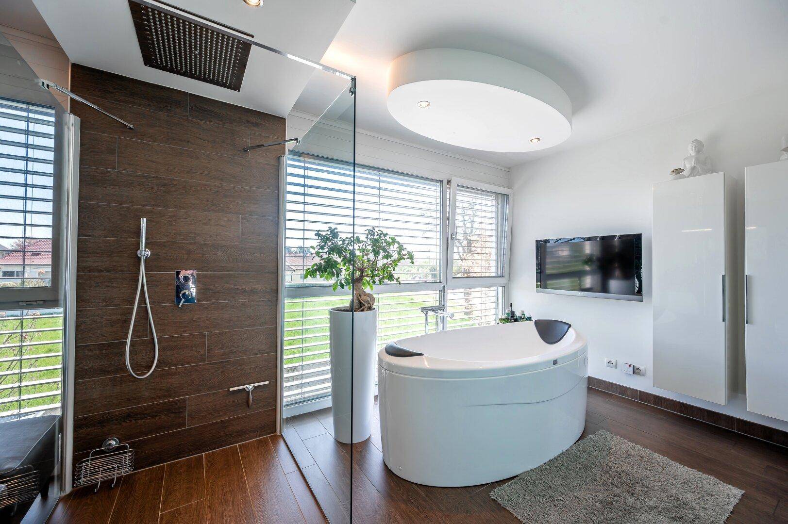 Modernes Badezimmer mit freistehender Badewanne, großer Regendusche und Fensterfront.