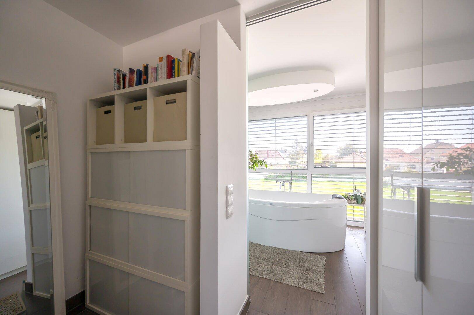 Heller Flur mit praktischem Regal und Blick in das moderne Badezimmer mit Badewanne.