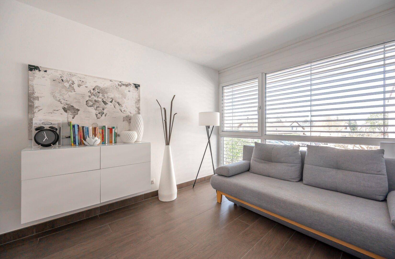 Helles Zimmer mit Sofa, Wandregal und großem Fenster, modern eingerichtet.
